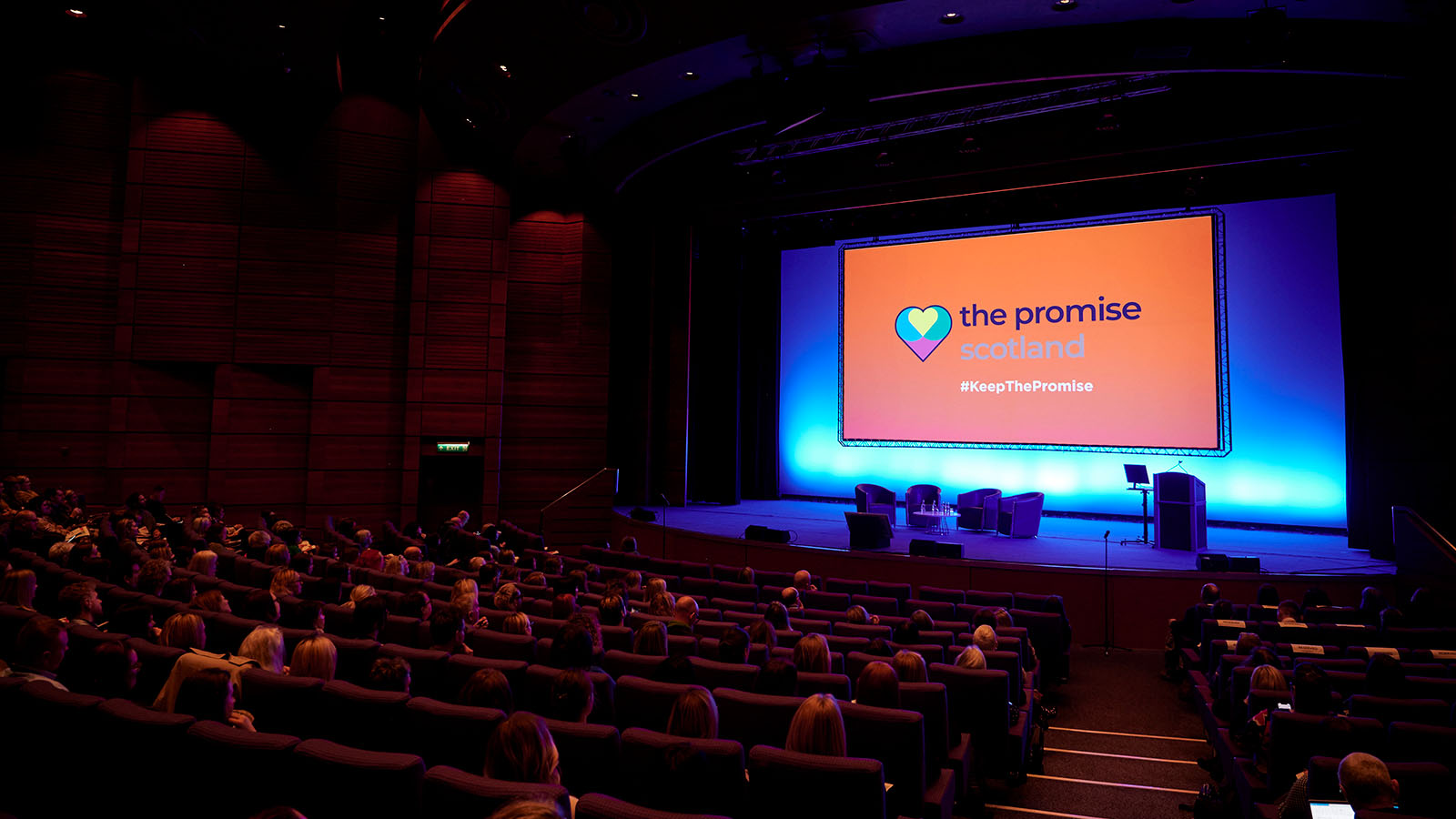 The logo of The Promise Scotland upon a large screen in a conference hall.